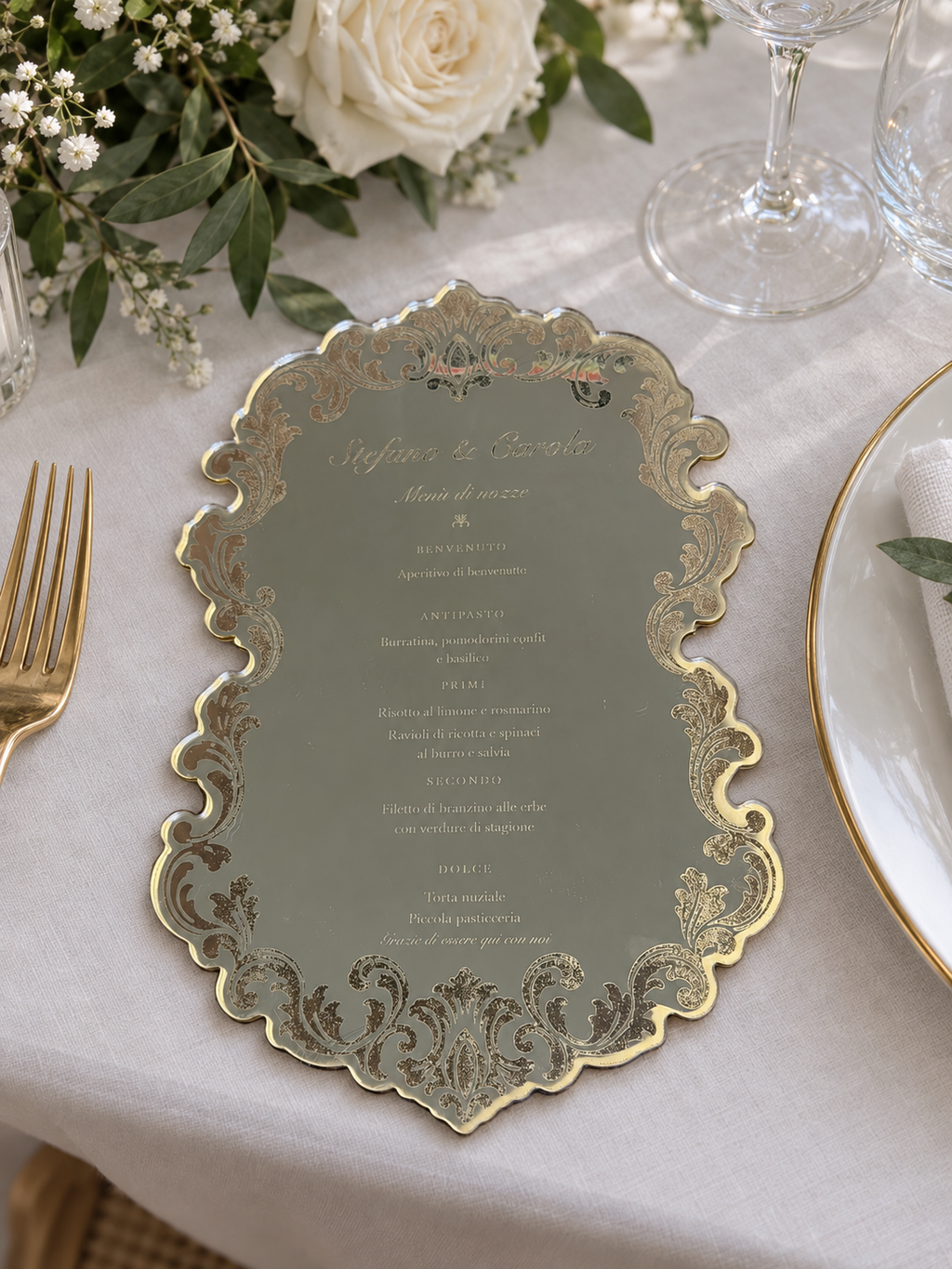 Menù personalizzato oro specchiato su tavola nuziale con fiori bianchi e posate dorate